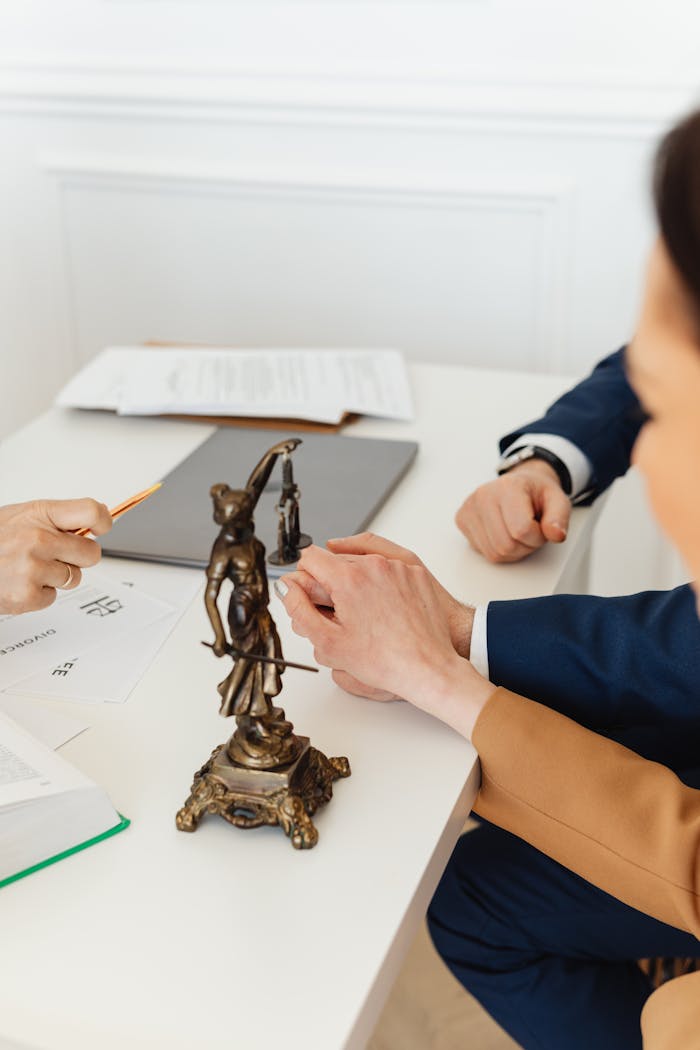 about-us Legal professionals discussing documents with Lady Justice statue on desk.